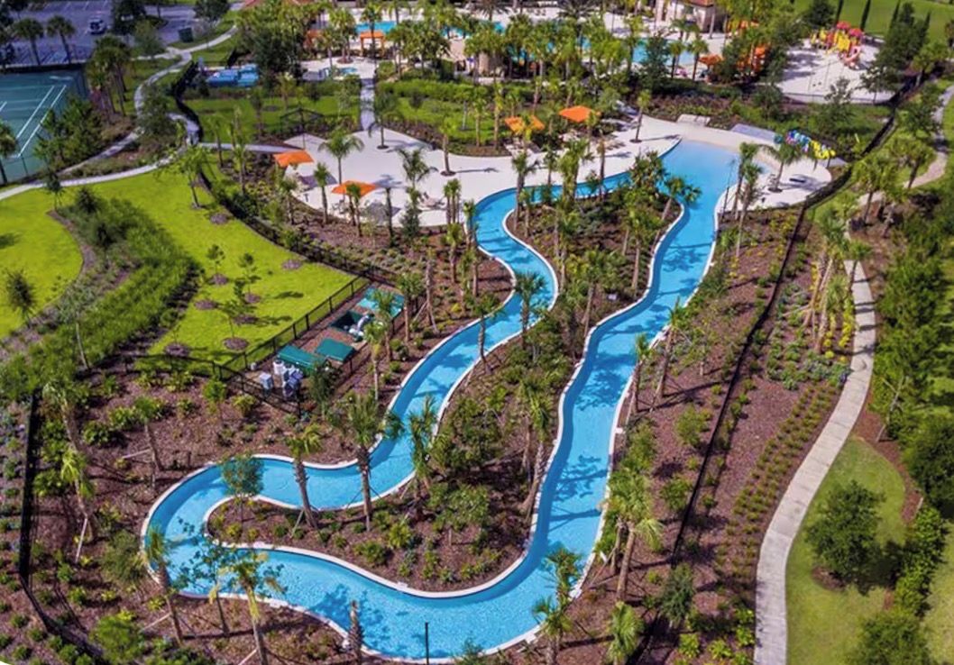 An aerial view of a resort with a winding pool, surrounded by palm trees and greenery.