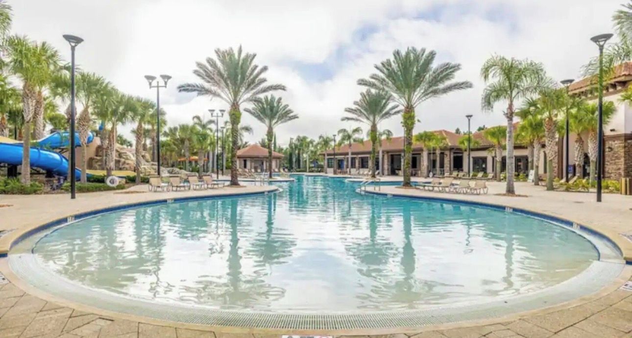 A swimming pool with a water slide, surrounded by palm trees and lounge chairs.