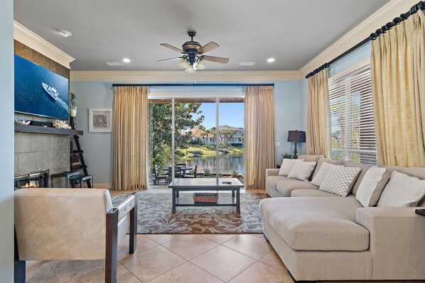 A living room with a sofa, coffee table, TV, fireplace, and a view of a lake.