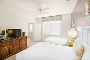 A bedroom with two beds, a ceiling fan, a television on a wooden dresser, and a window with blinds.