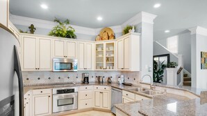 Una cocina moderna con armarios blancos, encimeras de granito, electrodomésticos de acero inoxidable y plantas decorativas.