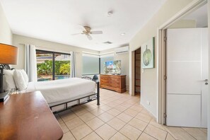 Une chambre à coucher comprenant un lit, un bureau, une commode, un ventilateur de plafond et donnant sur une piscine.