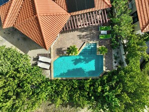 Vista aérea de un complejo turístico con piscina, rodeado de exuberante vegetación y una estructura de techo con tejas.