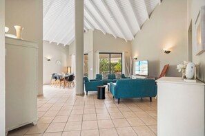 Un vaste espace de vie doté d’un haut plafond, un coin repas avec une table et des chaises, et un téléviseur posé sur un meuble.