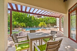 Une terrasse extérieure couverte avec une piscine, des chaises longues et une table avec des chaises.