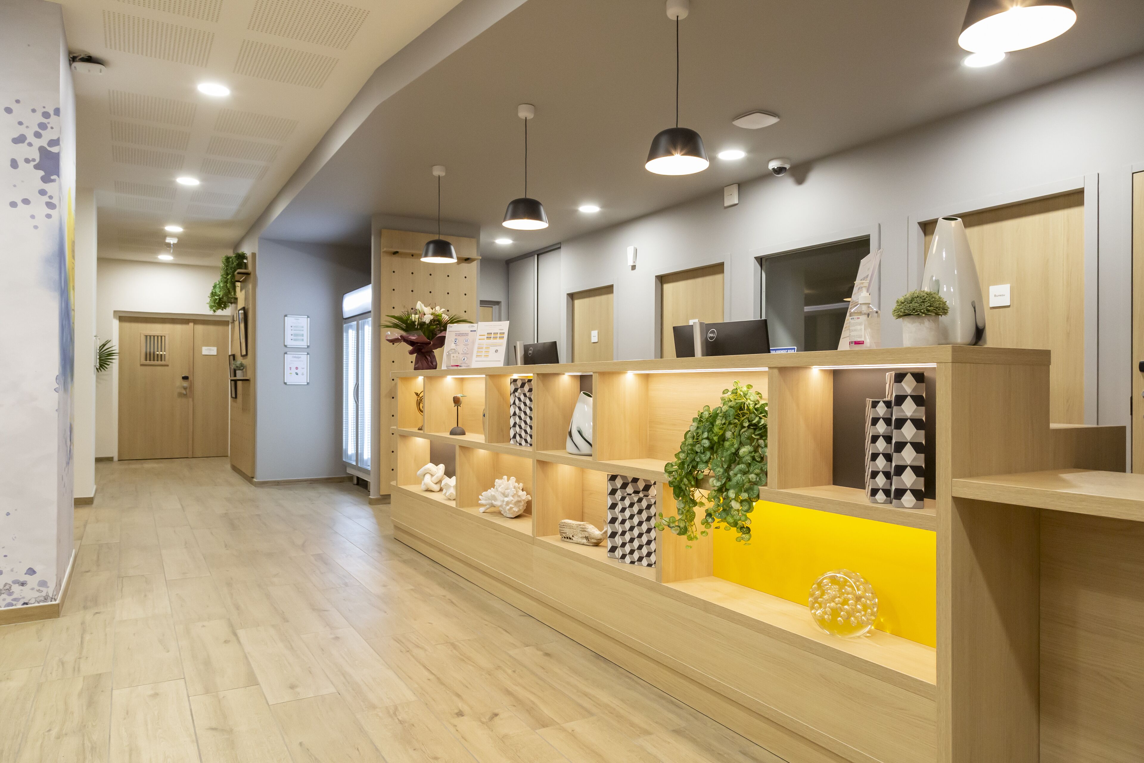 Una moderna recepción con suelo de madera, una barra central con varios objetos decorativos e iluminación colgante.