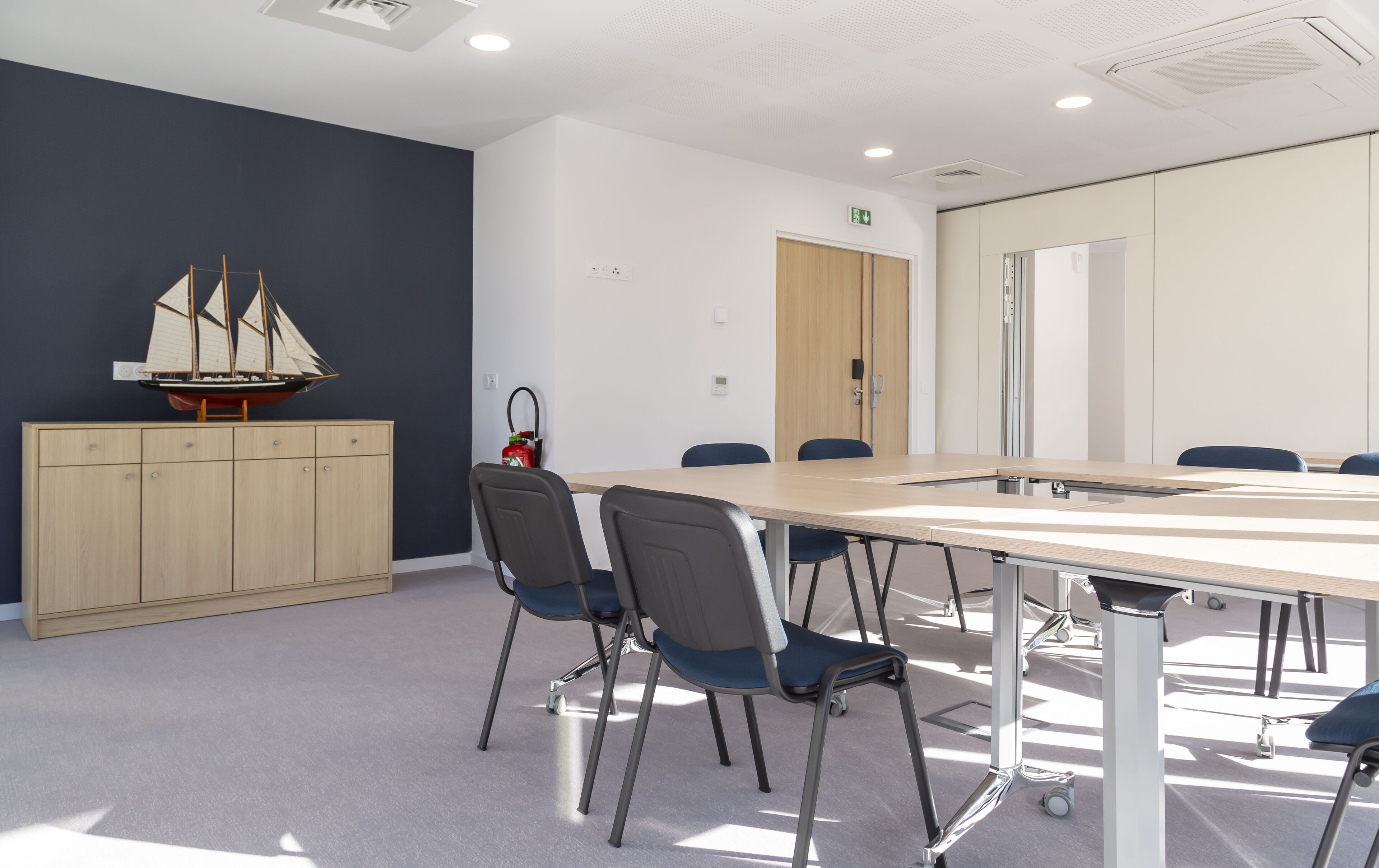 A conference room with a long table, chairs, a wooden cabinet, and a model ship.