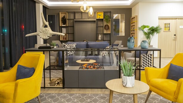 A modern living room with a glass coffee table, yellow chairs, a sofa, and decorative items. - Appart Hotel Odalys City Le Havre Centre (Le Havre)
