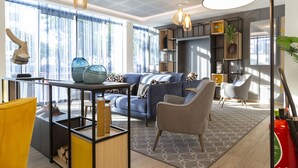 A modern living room with a blue sofa, a yellow chair, and a glass coffee table. There are pendant lights, a fireplace, and a bookshelf. - Appart Hotel Odalys City Le Havre Centre (Le Havre)