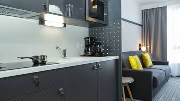 Una cocina moderna con microondas, cafetera y hervidor sobre la encimera. En la zona de estar hay un sofá gris con cojines amarillos.