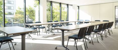 A conference room with a long table and chairs, large windows, and a view of buildings and trees outside.