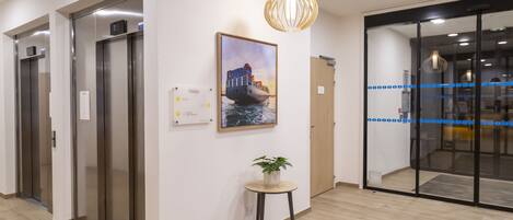 An interior with elevators, a painting of a ship, a plant on a table, and a modern light fixture.