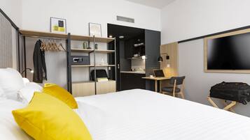 Habitación de hotel con cama, escritorio, silla, televisor y armario.
