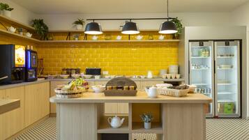 Una cocina moderna con azulejos amarillos, una isla central con vajillas de té y un refrigerador con puertas de vidrio.
