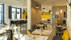 A modern restaurant with wooden tables and chairs, pendant lighting, and a yellow accent wall. - Appart Hotel Odalys City Le Havre Centre (Le Havre)