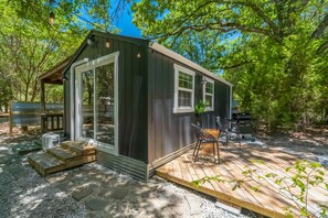 A small wooden cabin with a porch, large windows, and a grill outside.