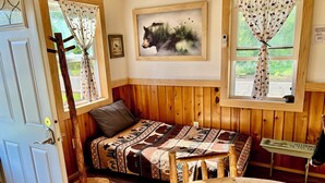 Una habitación cálida tipo cabaña con una cama de madera, una mesita pequeña y un cuadro de un oso en la pared.