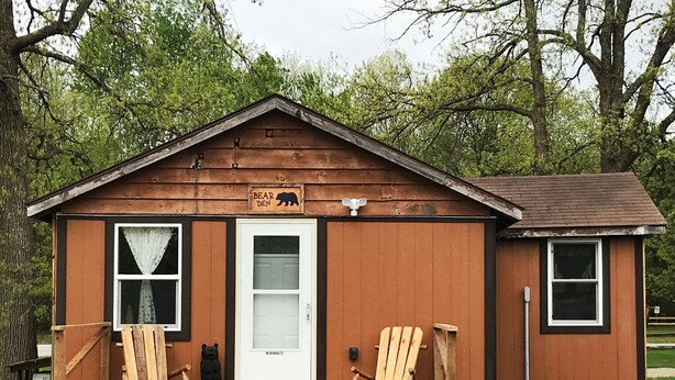 Una pequeña cabaña de madera con un letrero de oso, dos sillas de madera y una puerta con un letrero que indica 'No fumar'.
