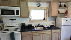 Cocina compacta con armarios de madera, estufa, microondas, lavamanos y refrigerador.