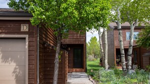 Une maison en bois avec un garage, une véranda et un jardin bien entretenu, agrémenté d’arbres et de plantes.