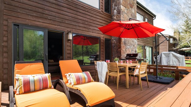 Une terrasse extérieure aménagée avec du mobilier en bois, comprenant des chaises longues et une table avec des chaises, ainsi qu’un parasol rouge.