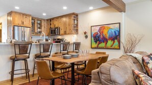Une cuisine moderne avec des meubles en bois, des appareils électroménagers en acier inoxydable et un coin repas comprenant une table et des chaises en bois.