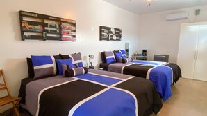 A hotel room with two beds, a ceiling fan, a wall-mounted air conditioner, and a decorative rug. - Carmen's Marfa Hotel/Tomas 2 Queen Beds (Marfa)