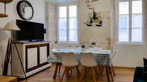 Een eethoek met een tafel gedekt voor twee personen, een televisie op een kast en een decoratie van een zeilboot aan de muur.