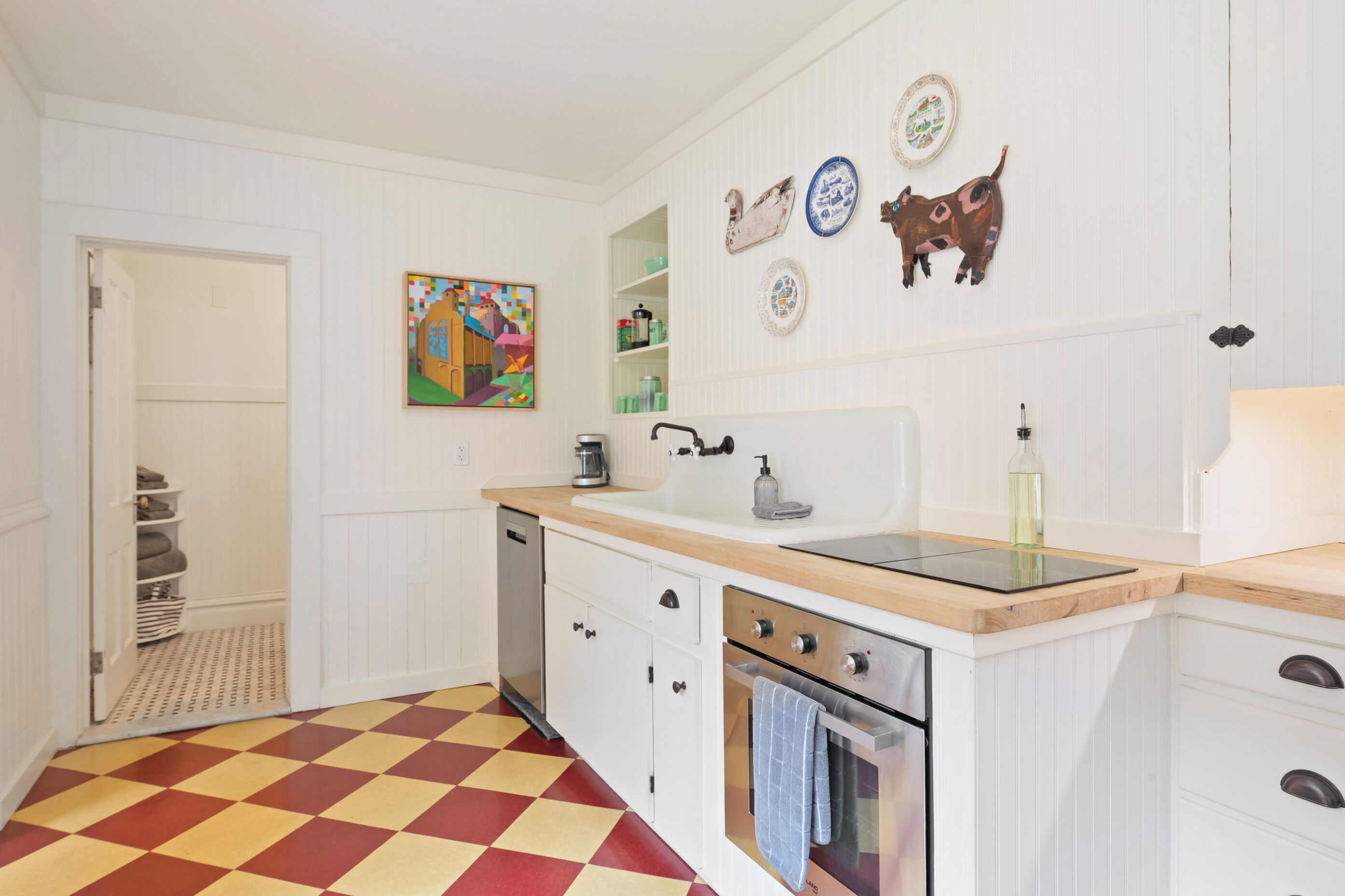 A kitchen with a checkered floor, white cabinetry, a coffee machine, and decorative plates on the wall.
