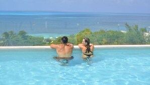 Una pareja descansando en una piscina con vistas al océano y paisaje tropical.