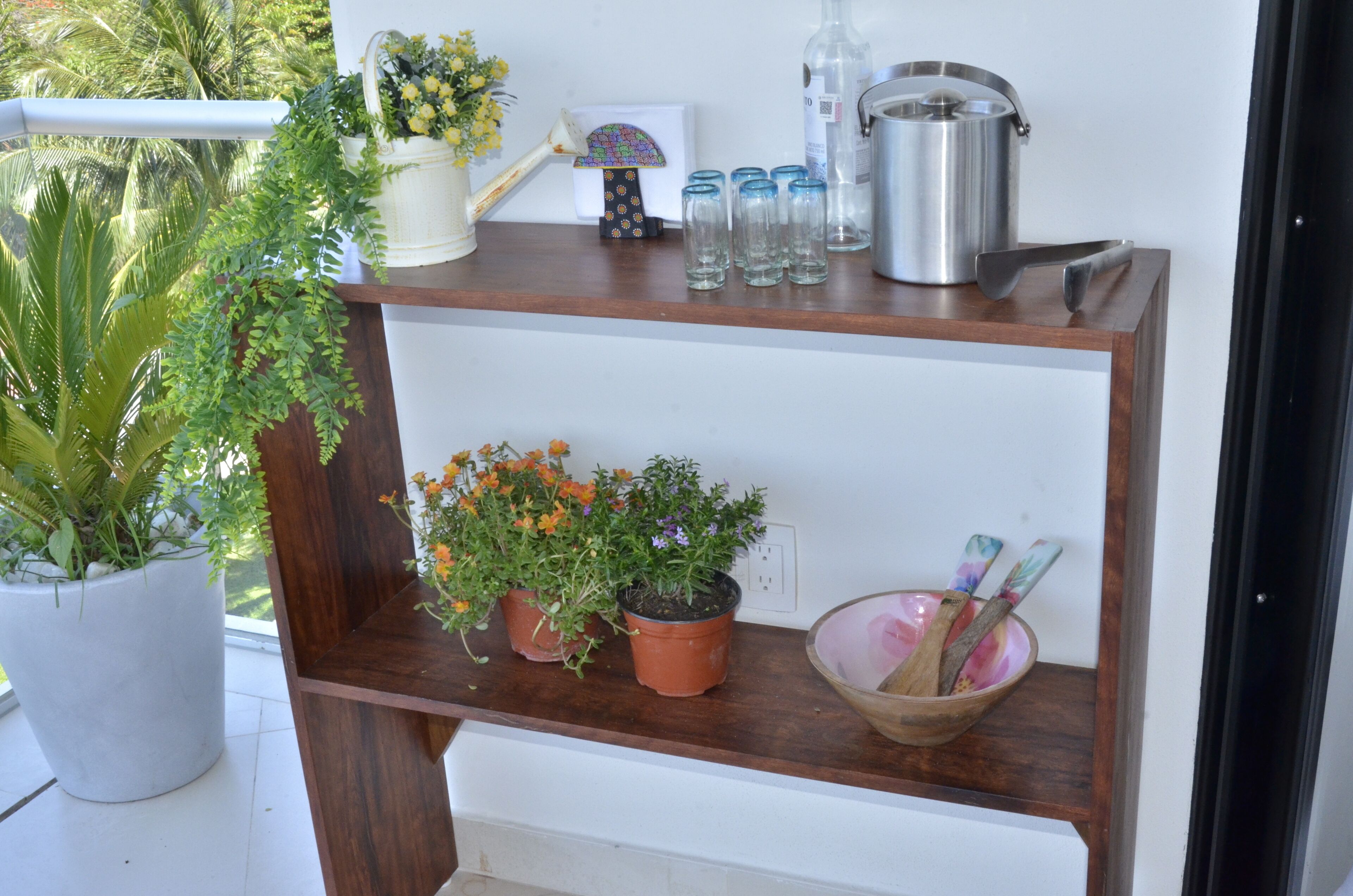 A wooden shelf with potted plants, a bowl with wooden utensils, and kitchenware.