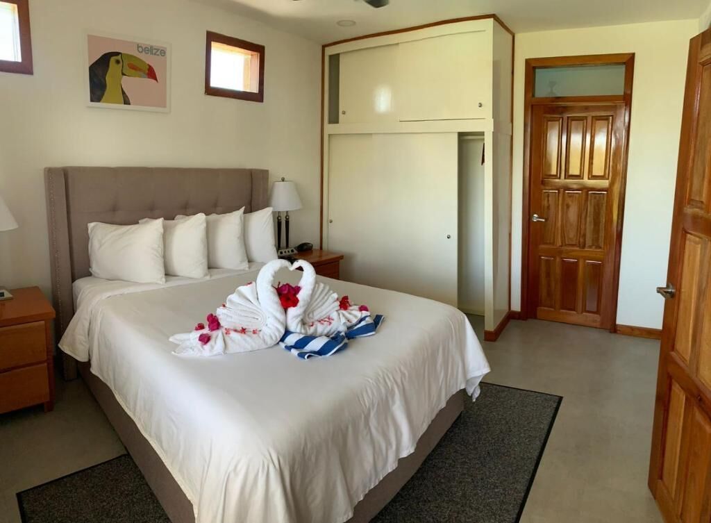 Una habitación de hotel con una cama grande, un armario de madera, una mesita de noche con lámpara y un aire acondicionado instalado en la pared.