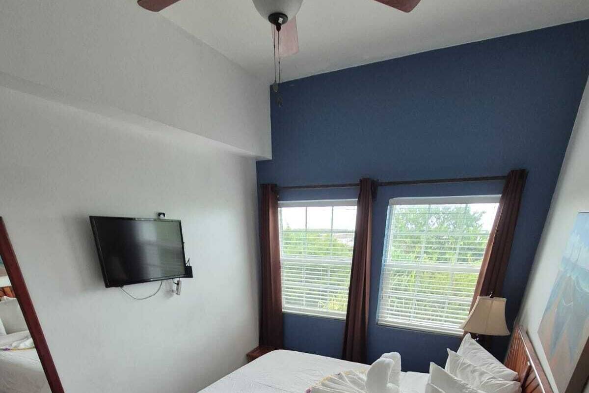 Ein Hotelzimmer mit Bett, Fernseher, Schreibtisch, Lampe und einem Fenster mit Vorhängen.