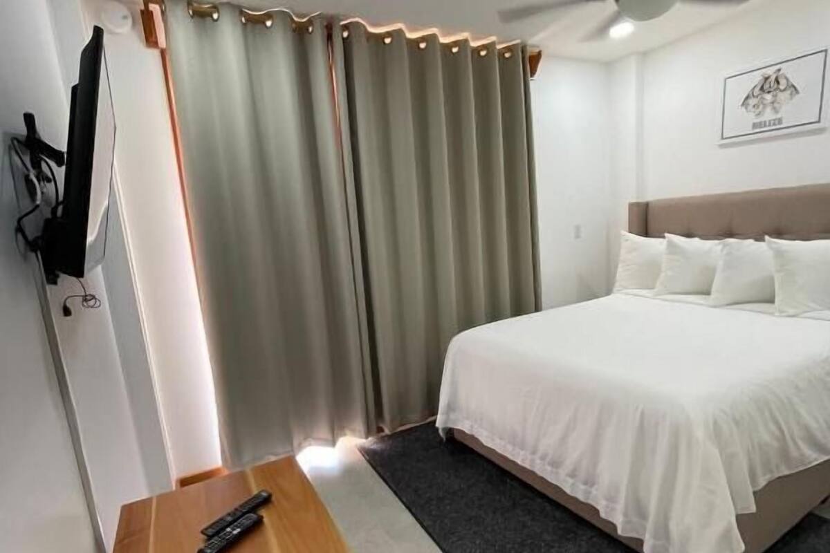 Ein Hotelzimmer mit einem Bett, einem Nachttisch aus Holz, einem Deckenventilator und einem an der Wand befestigten Fernseher.