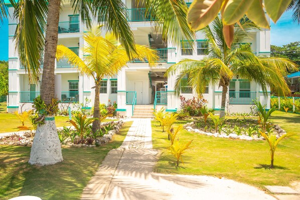 A multi-story hotel with a central staircase, surrounded by palm trees and a well-maintained lawn.