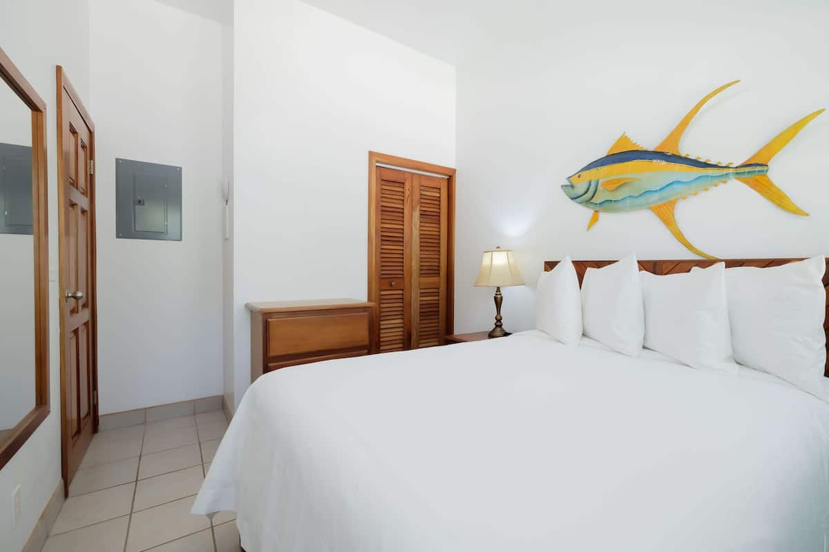 Ein Hotelzimmer mit einem Bett, einem Nachttisch aus Holz, einer Lampe, einer Wanddekoration mit Fischen und einer Tür mit Spiegel.
