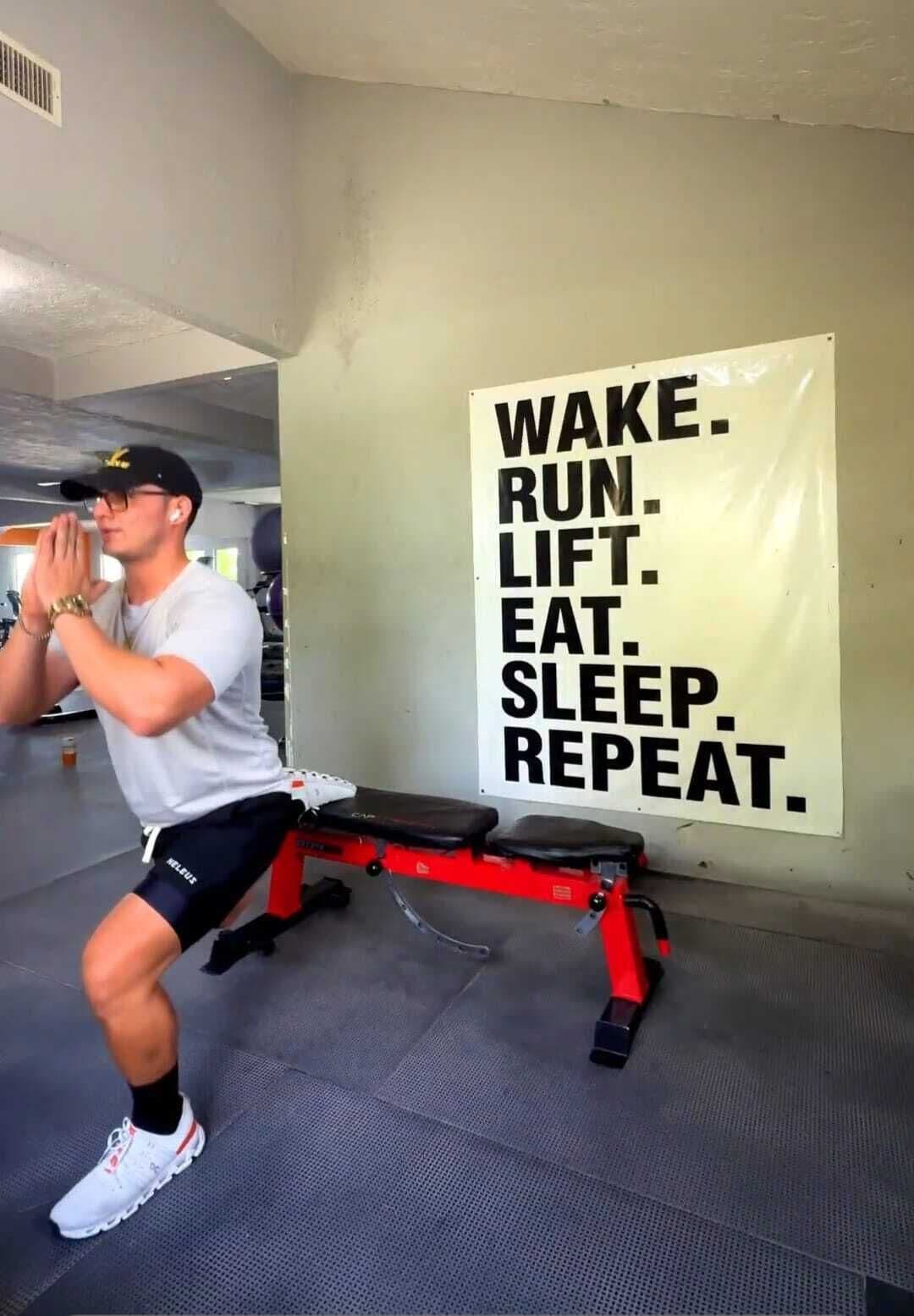 Una persona ejercitándose en un banco dentro de un gimnasio, con un cartel motivacional en la pared.
