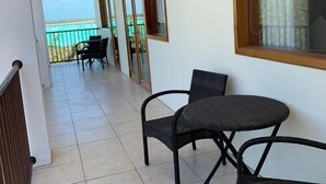 A balcony with two wicker chairs and a table, a view of the sea, and a tiled floor.