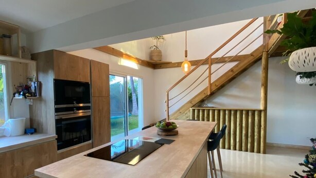 Una cocina moderna con una isla central, electrodomésticos integrados y una escalera de madera.