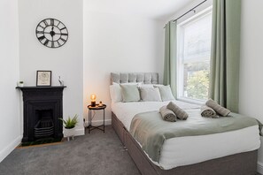 Quarto com cama, lareira, relógio de parede e janela com cortinas.