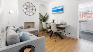 A modern living room with a grey sofa, a dining table with chairs, a large window with a view of the sea, and a kitchen area with white cabinets. - City Reach (Exeter)