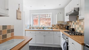 A modern kitchen with white cabinets, a tiled backsplash, a window with a view, a gas stove, and a sink. - City Reach (Exeter)