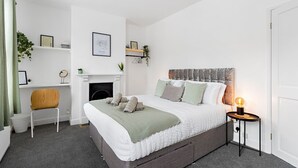 A bedroom with a bed, a chair, a fireplace, and a nightstand with a lamp. - City Reach (Exeter)