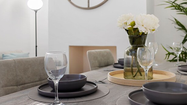 A dining table set with plates, bowls, and wine glasses, a vase with flowers, and a lamp in the background. - City Reach (Exeter)