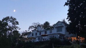 Et stort, tosset etagehus med en markant skorsten, omgivet af træer og en velholdt have.