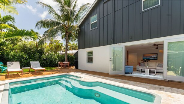 A swimming pool with lounge chairs, a patio, and a building with a dark exterior and glass doors. - OFF THE HOOK - 3 Bedroom / 3 Bathroom W/ Pool & Parking (Key West)