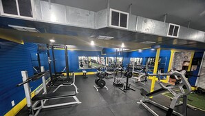 Un gimnasio con diversos equipos de ejercicio, incluyendo máquinas de pesas y pesas libres, en una distribución amplia.