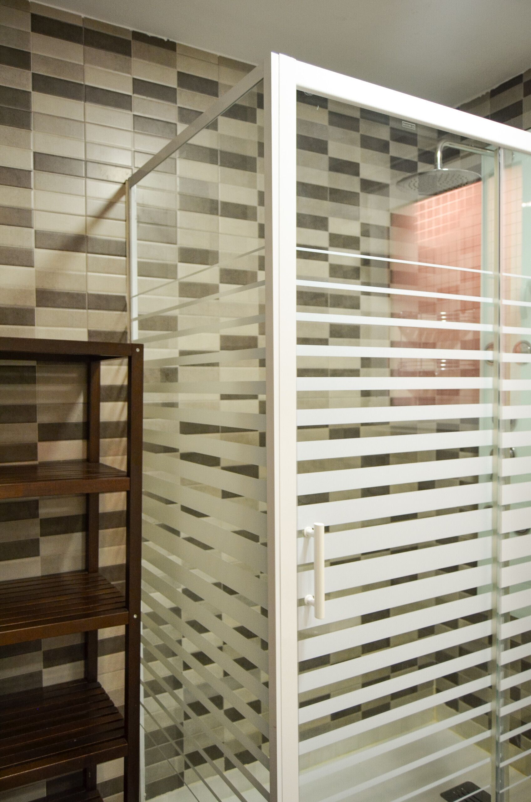 A bathroom with a tiled wall, a wooden bench, and a glass partition.