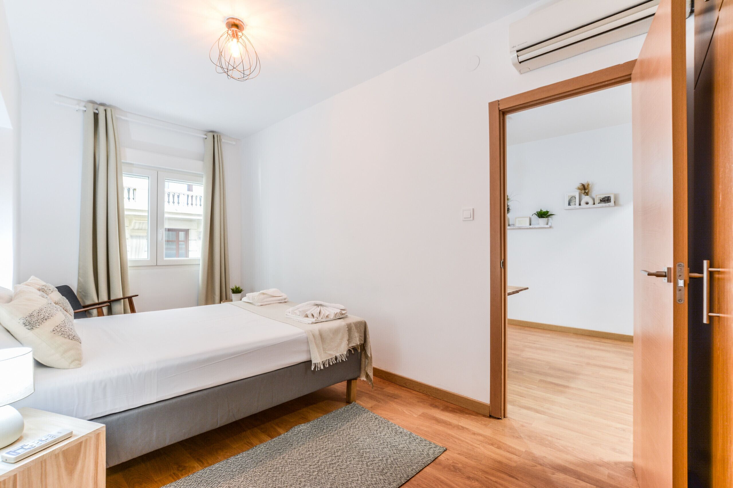 Une chambre à coucher avec un lit, une table de chevet, une lampe et une vue sur l’extérieur par une fenêtre.