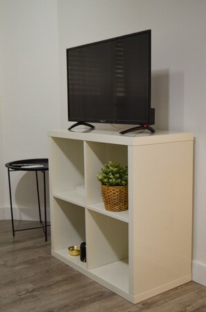 Un téléviseur posé sur un meuble blanc doté d’étagères, une petite table et une plante.